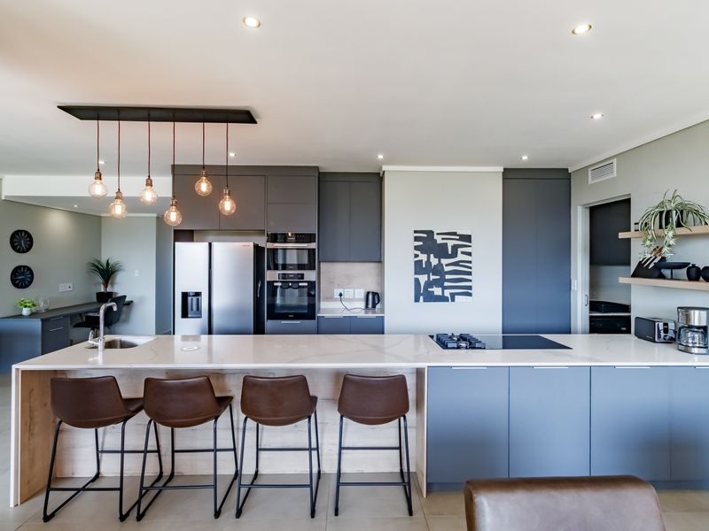 Modern open-plan kitchen featuring a large island with stone countertops, integrated appliances, sleek cabinetry, and stylish pendant lighting in a contemporary apartment setting.