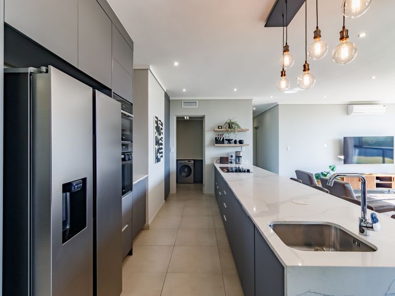 Modern open-plan kitchen featuring a large stone island, sleek cabinetry, integrated appliances, and seamless flow into the living area.
