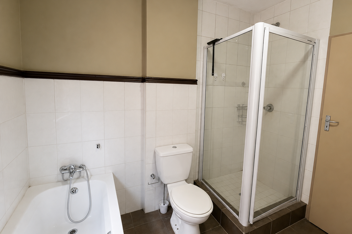 A functional bathroom featuring a built-in bathtub, a separate glass-enclosed shower, and a standard toilet with neutral wall tiling.