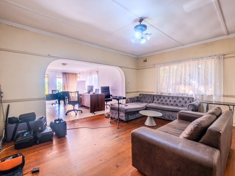 Spacious open-plan living area featuring original hardwood flooring, a classic archway transition, and a ceiling fan, offering a versatile layout for various living arrangements.