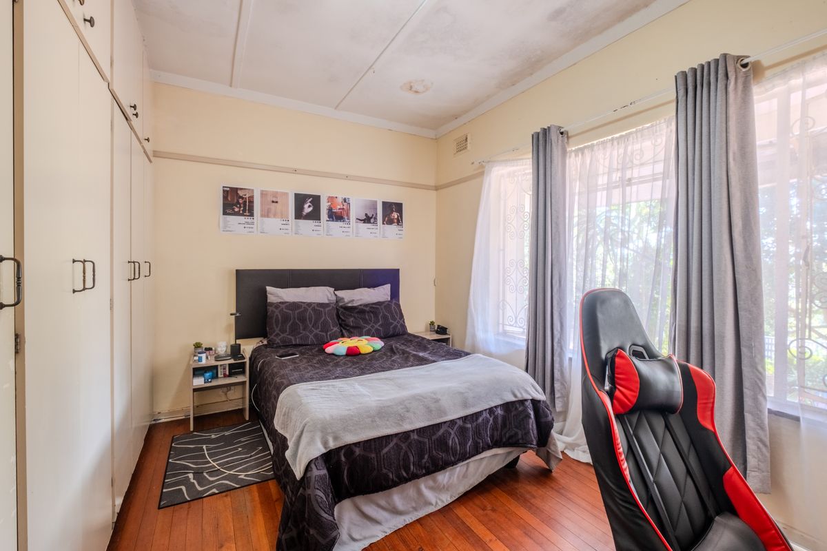 Bedroom featuring hardwood flooring, built-in cupboards, and security gates on windows. The ceiling shows signs of water damage requiring repair.