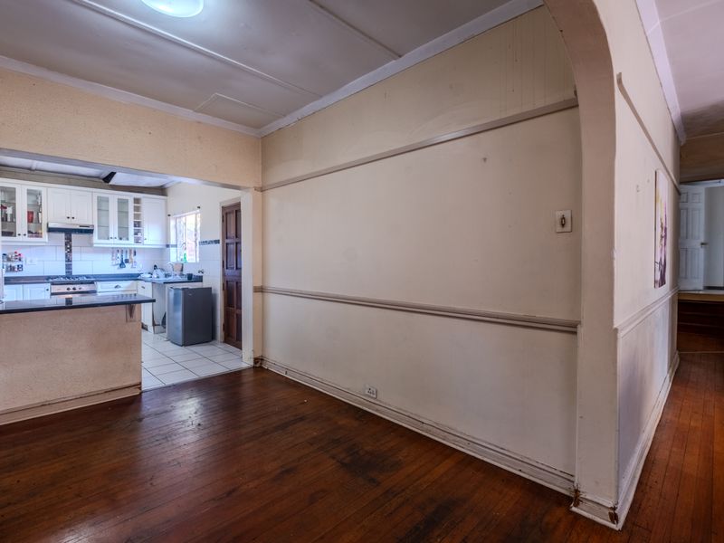 Open plan living area featuring hardwood floors and an adjoining kitchen with built-in cabinetry, gas hob, and extractor fan.