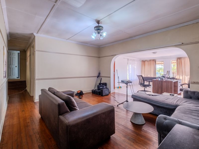 Open plan living area featuring original hardwood flooring, a central archway, and classic picture rails, offering a versatile space for renovation.