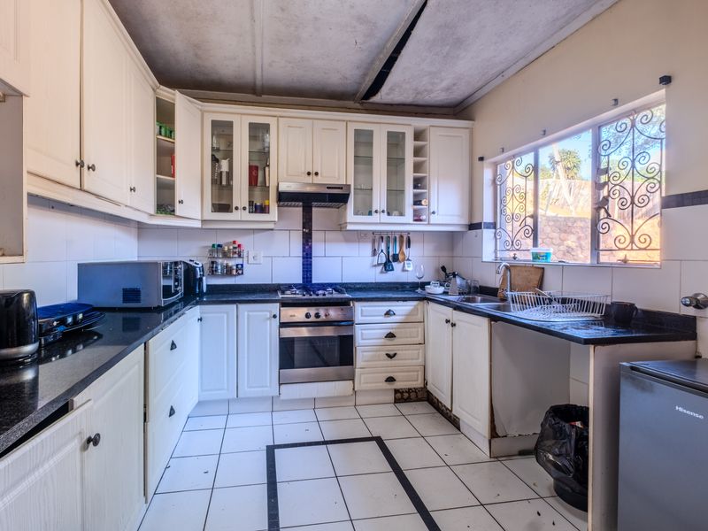 A functional kitchen featuring built-in cabinetry, granite countertops, and integrated appliances, requiring ceiling repairs and cosmetic updates to modernize the space.