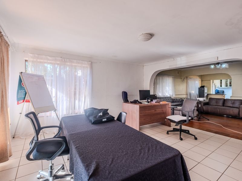 Open-plan living area featuring tiled and hardwood flooring, connected by a classic archway, with visible ceiling and wall maintenance required.