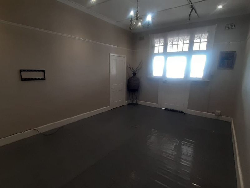 An empty living room featuring timber flooring, picture rails, and a multi-pane window, requiring minor cosmetic updates and electrical repairs.