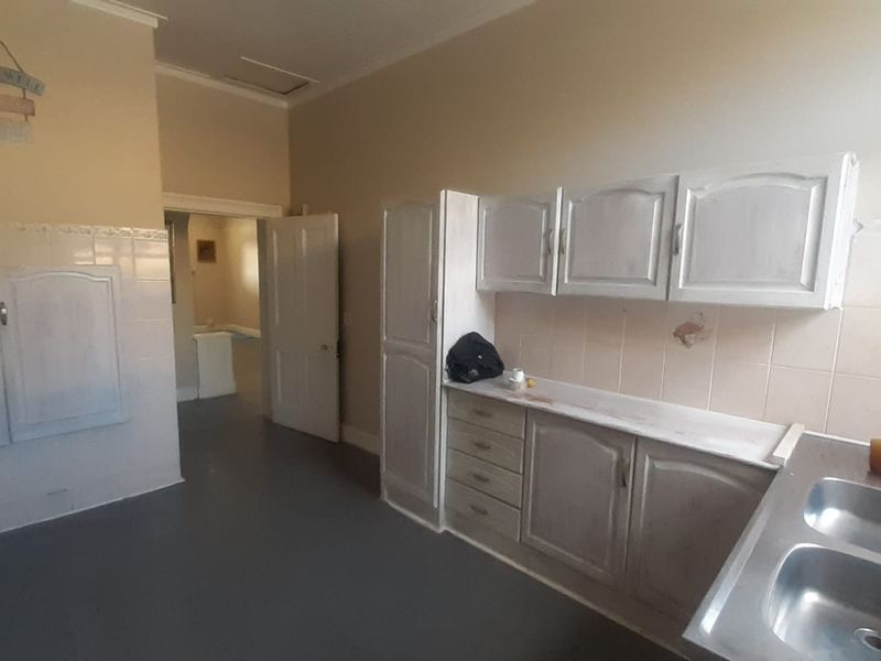 A dated kitchen area featuring built-in cabinetry, a double bowl stainless steel sink, and tiled splashbacks, offering potential for renovation and modernization.