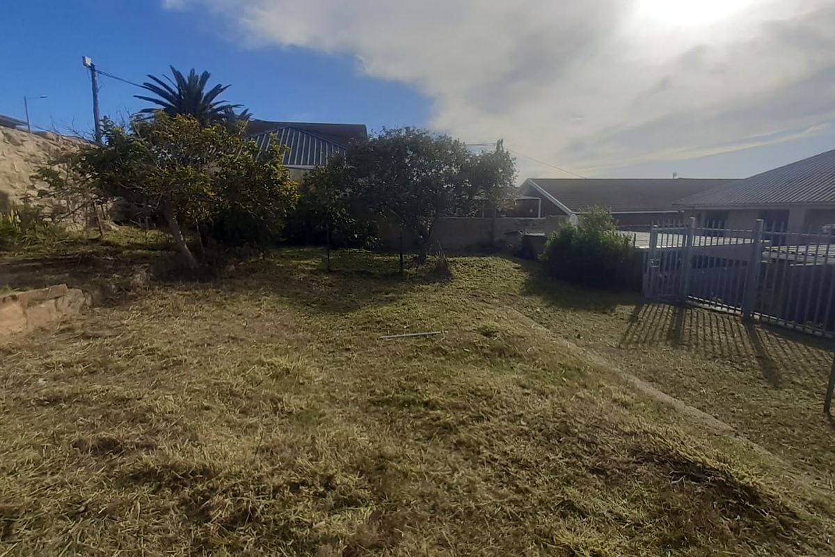 A rear garden area featuring a retaining wall, metal security fencing, and a gate, with an uneven, grassed surface.