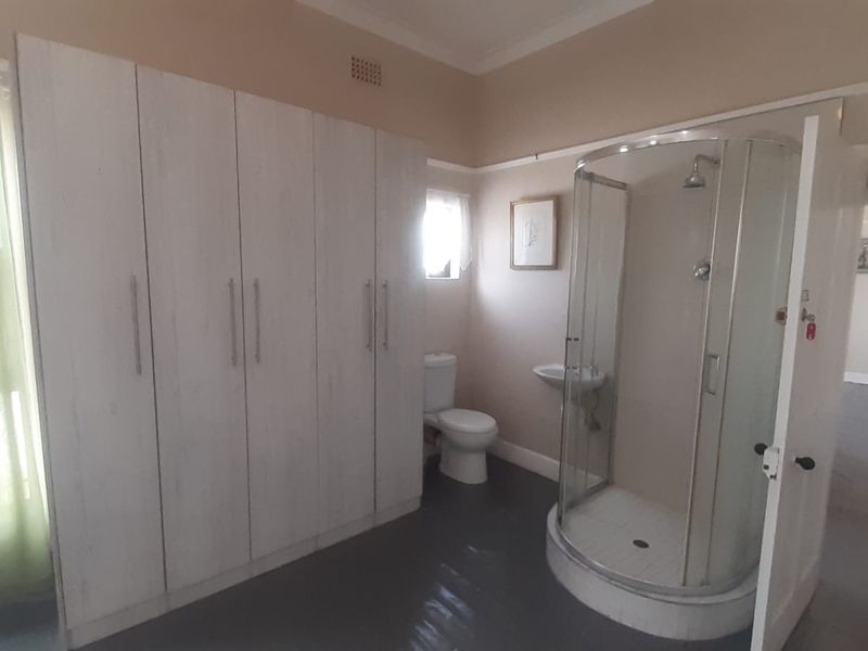 A functional bathroom featuring a corner shower enclosure, toilet, wall-mounted basin, and extensive built-in storage cupboards with a neutral finish.