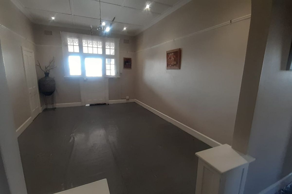 An empty living room featuring painted floorboards, picture rails, and a classic timber-framed door with glass panels.