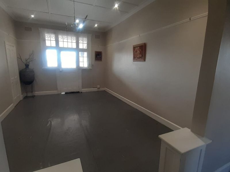 An empty living room featuring painted floorboards, picture rails, and a classic timber-framed door with glass panels.