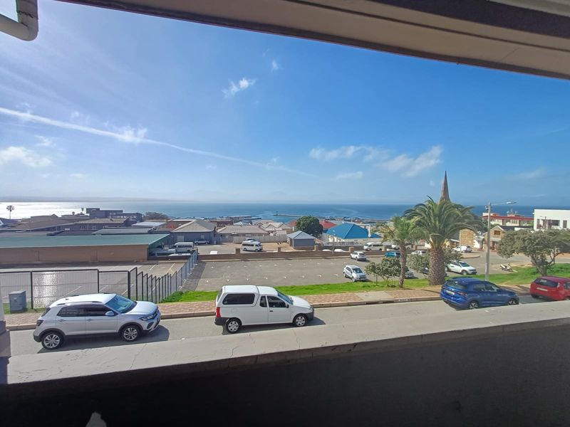 An elevated view overlooking the surrounding neighbourhood, parking area, and distant ocean coastline.