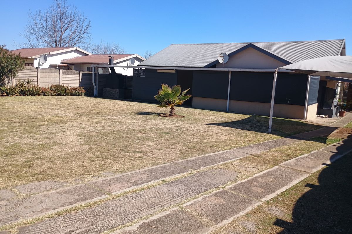 Rear view of the property featuring a spacious lawn, concrete driveway, and a covered patio area with a corrugated metal roof.