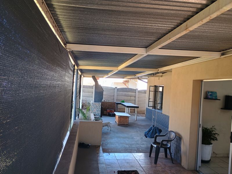 Covered outdoor patio area featuring a built-in braai, tiled flooring, and a corrugated metal roof structure, providing a functional space for outdoor entertaining.
