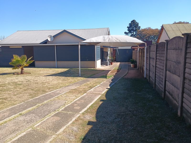 Rear exterior view of the property featuring a concrete driveway, a shade sail structure, and a precast concrete boundary wall.