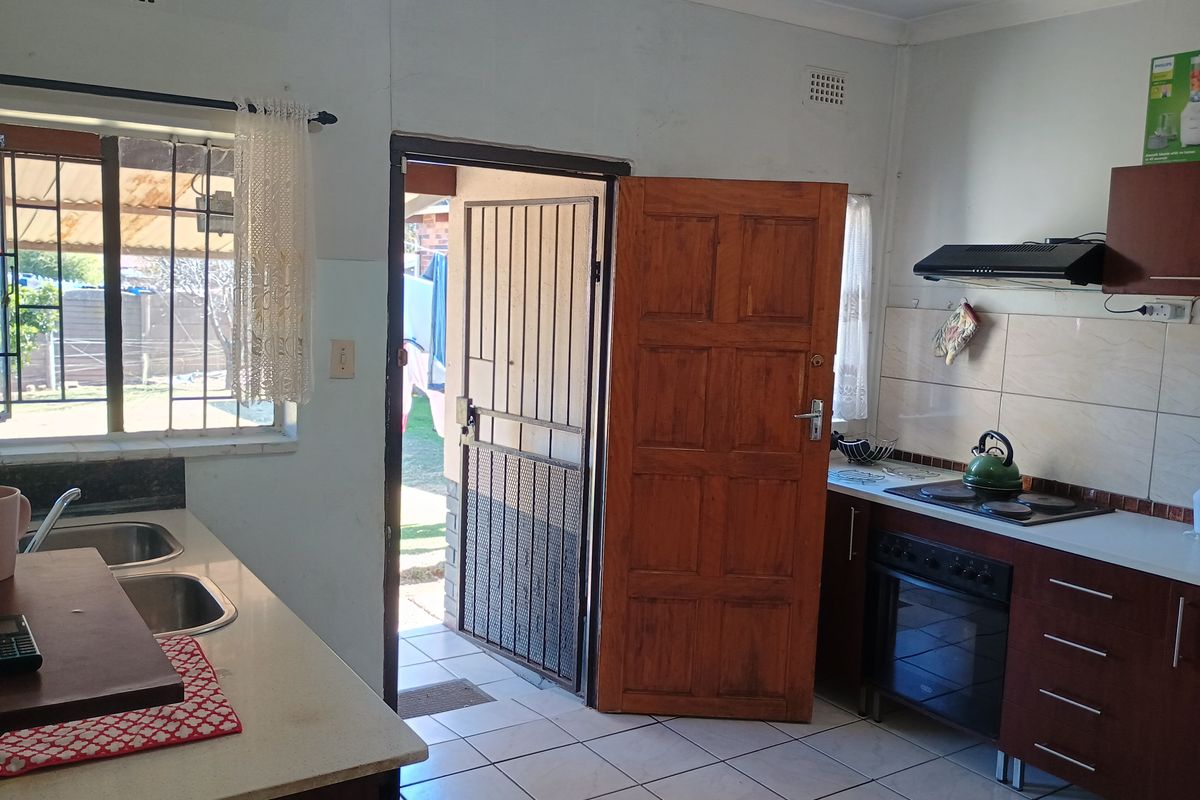 Functional kitchen featuring built-in cabinetry, electric hob, oven, and extractor fan, with direct access to the exterior through a security gate.