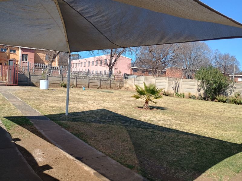 Spacious backyard featuring a large lawn, paved walkway, and a shade sail structure, enclosed by a precast concrete boundary wall.