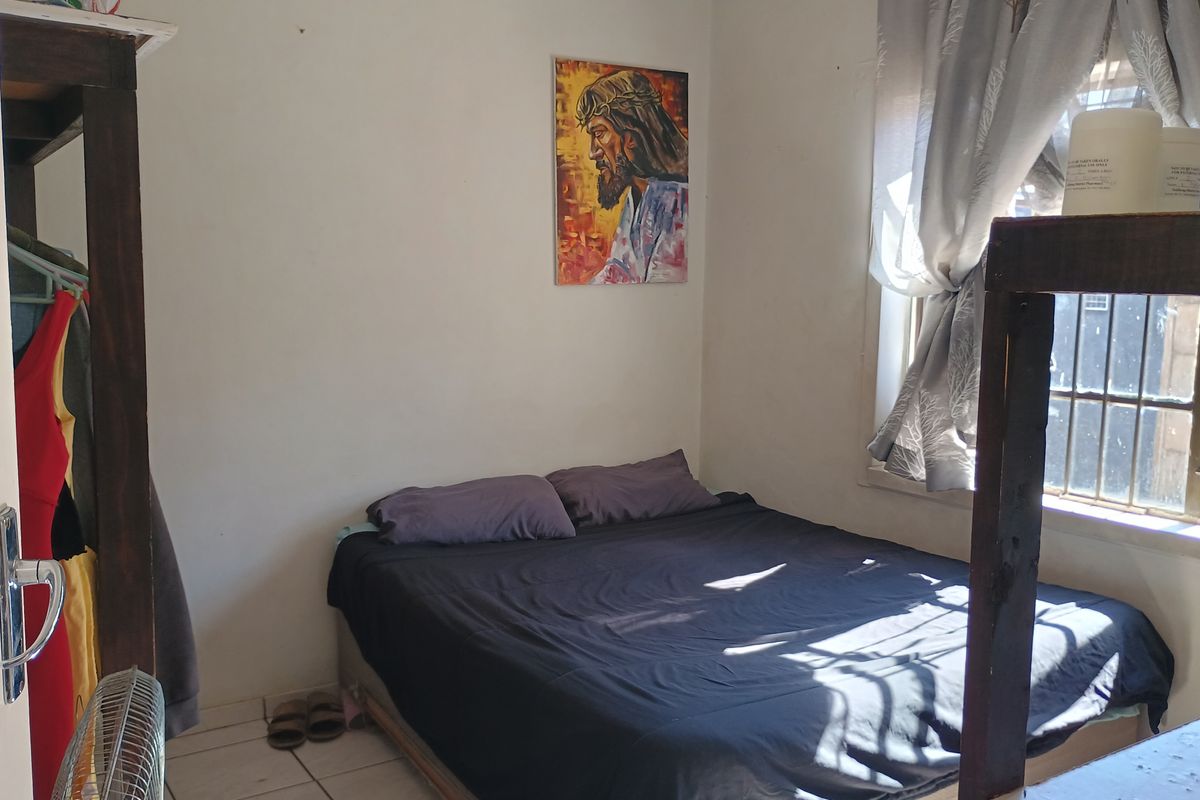 A compact bedroom featuring tiled flooring and a window fitted with security bars, offering a functional space with potential for cosmetic updates.