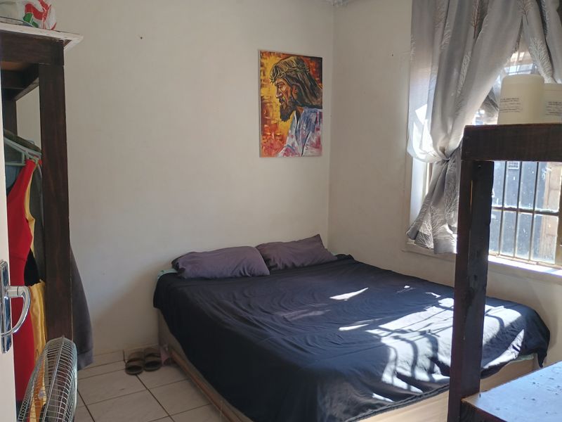 A compact bedroom featuring tiled flooring and a window fitted with security bars, offering a functional space with potential for cosmetic updates.