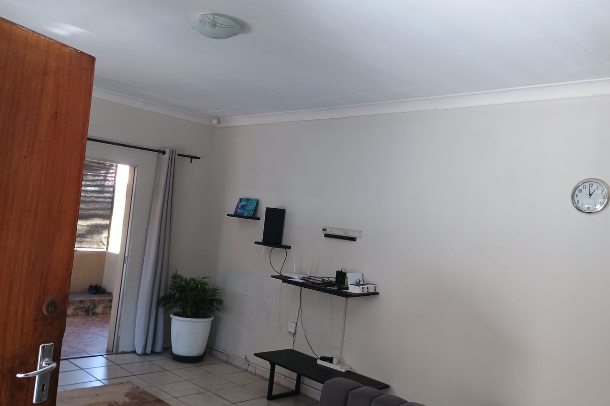 A living room area featuring tiled flooring, cove cornicing, and neutral wall finishes, providing a functional space with direct access to an outdoor area.