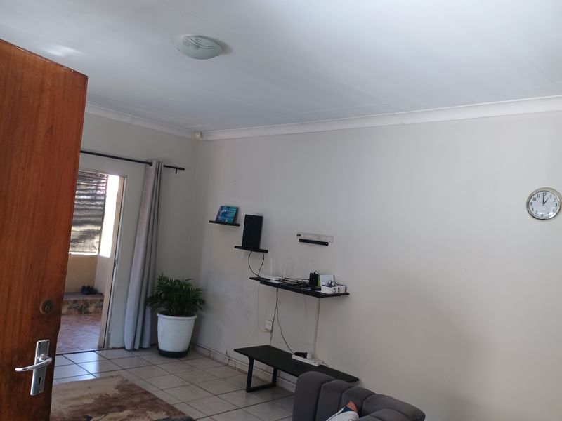A living room area featuring tiled flooring, cove cornicing, and neutral wall finishes, providing a functional space with direct access to an outdoor area.