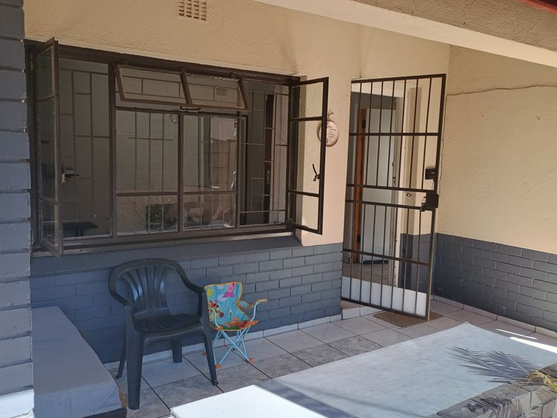 A covered patio area featuring tiled flooring, security gate, and security bars on the window, with a brick-accented exterior wall.