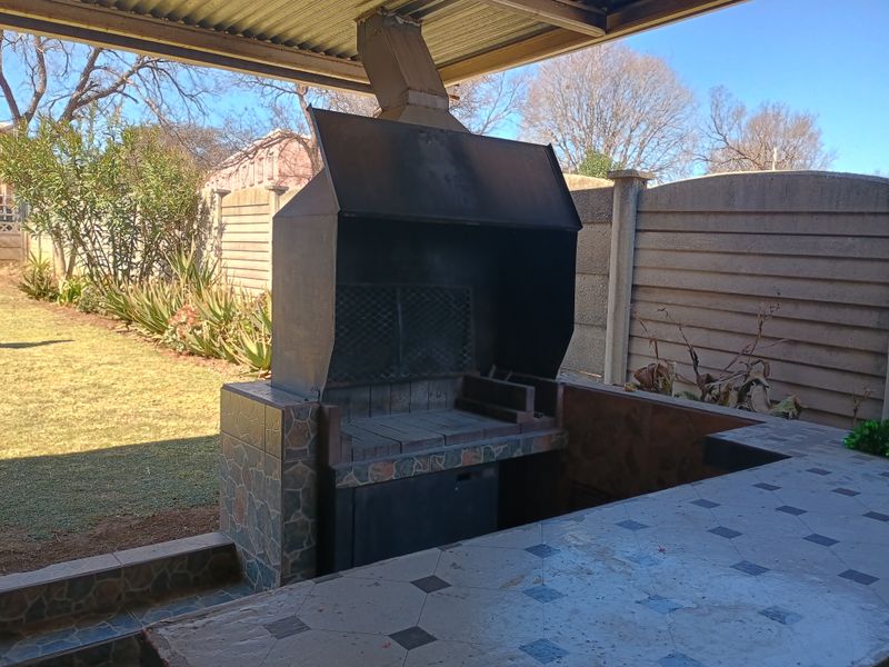 Covered outdoor patio area featuring a built-in braai and tiled preparation counter, overlooking the rear garden.