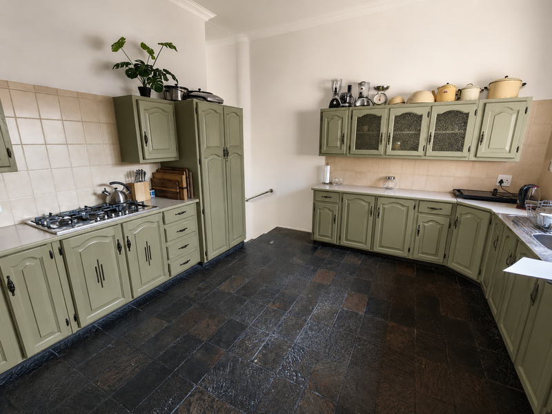 A functional kitchen featuring sage green cabinetry, a gas hob, tiled splashbacks, and dark stone floor tiles.