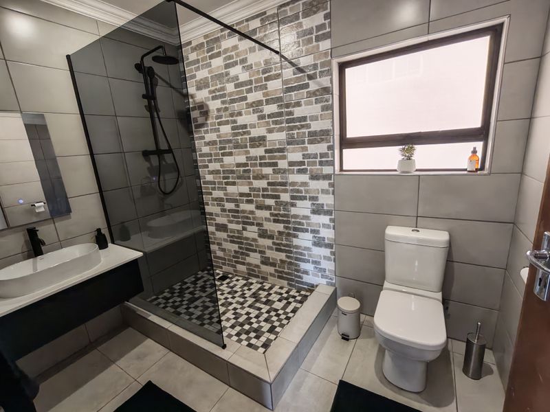 Modern bathroom featuring a walk-in shower with a glass screen, wall-mounted vanity with a vessel sink, and contemporary tiled finishes.