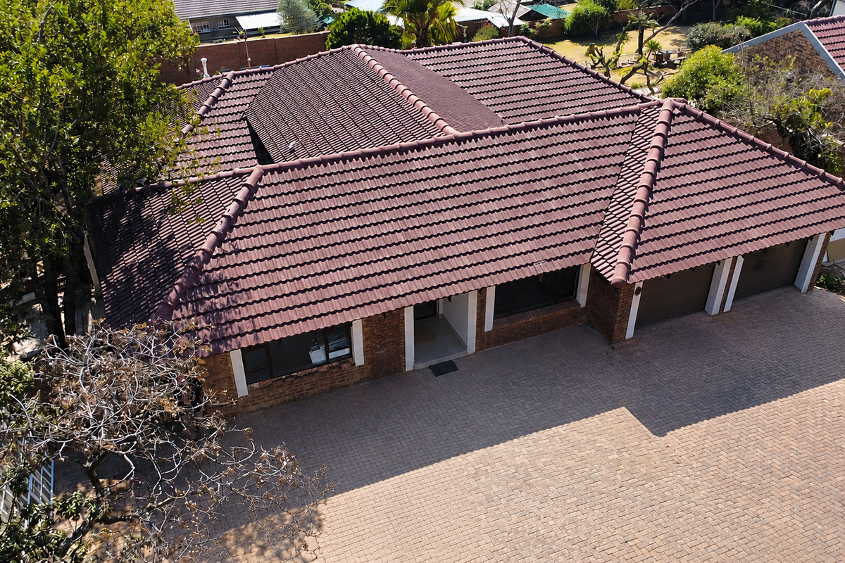 Aerial view of a residential property featuring a tiled roof, brick exterior, and a spacious paved driveway leading to a triple garage.