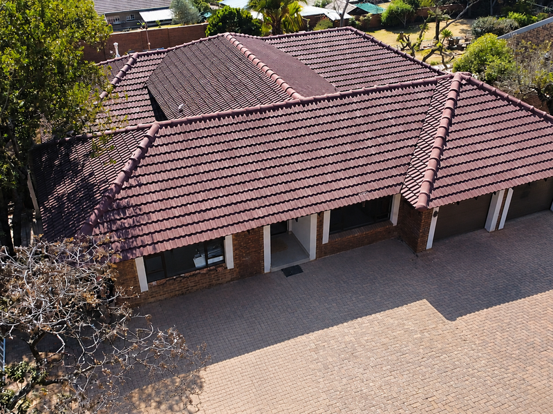Aerial view of a residential property featuring a tiled roof, brick exterior, and a spacious paved driveway leading to a triple garage.