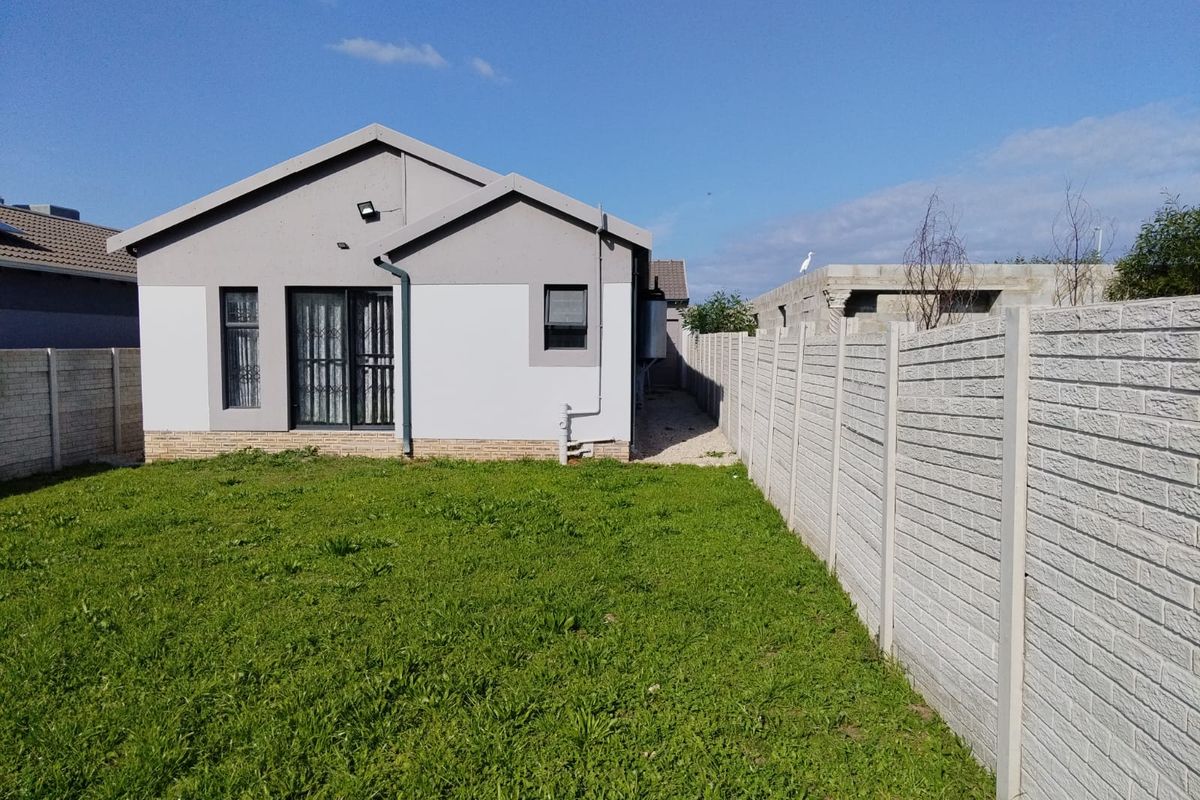Rear view of the house featuring a lawn, precast concrete boundary wall, and a sliding glass door with security gate.