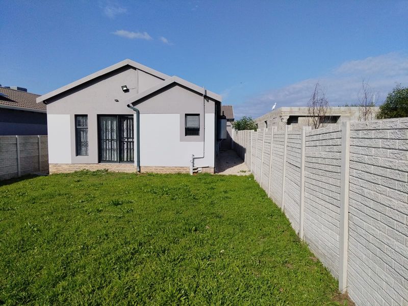 Rear view of the house featuring a lawn, precast concrete boundary wall, and a sliding glass door with security gate.
