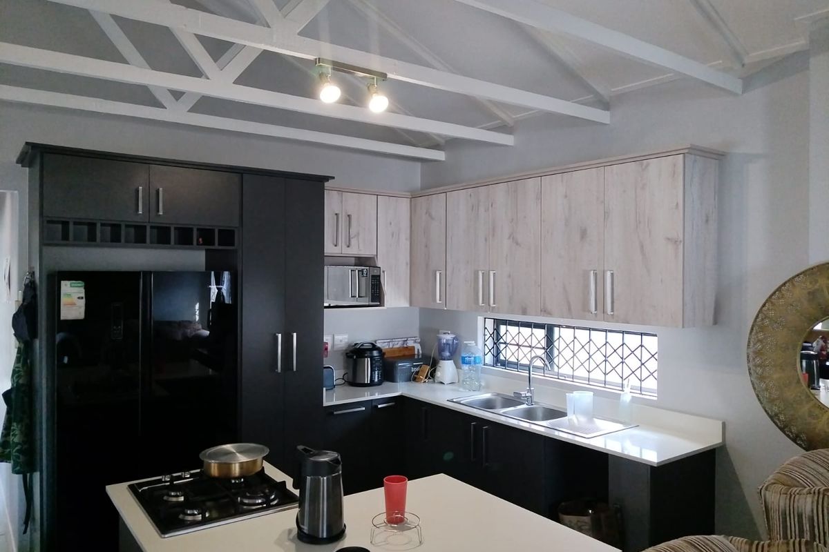 Modern kitchen featuring two-tone cabinetry, stone countertops, a central island with a gas hob, and exposed white ceiling beams.
