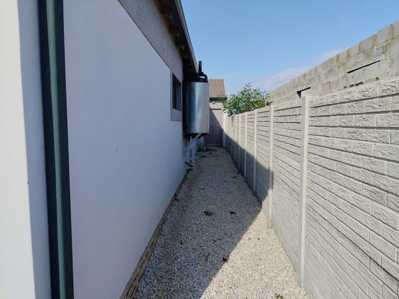 A narrow side passage featuring a precast concrete boundary wall, gravel ground cover, and an external geyser unit.