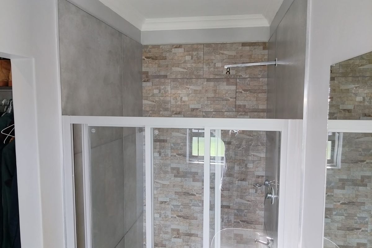 A modern shower area featuring a glass enclosure, rain shower head, and a combination of stone-look and large format grey wall tiles.