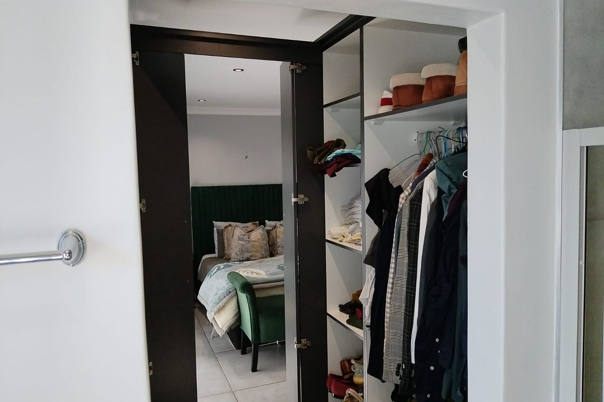 A view through a doorway into a bedroom featuring tiled floors, recessed lighting, and a built-in wardrobe with shelving and hanging space.