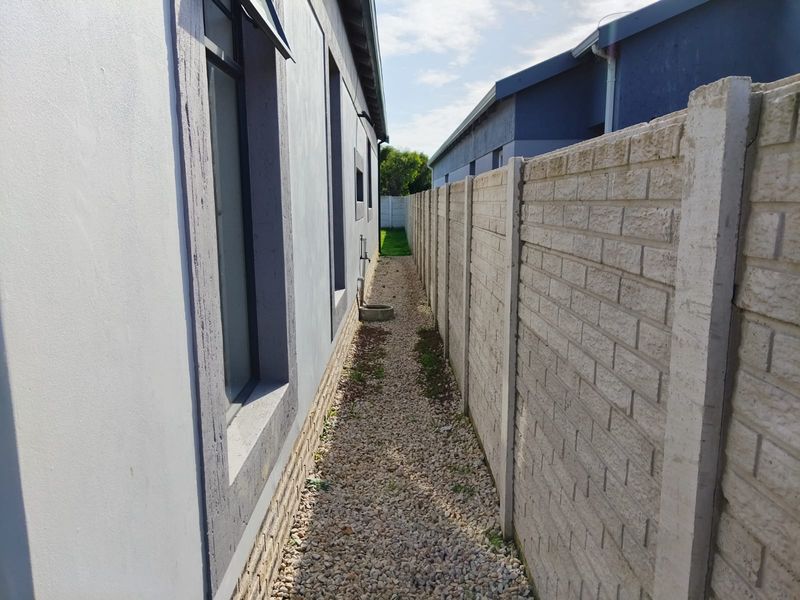 A narrow side passage featuring a gravel pathway, precast concrete boundary wall, and external water tap along the side of the house.