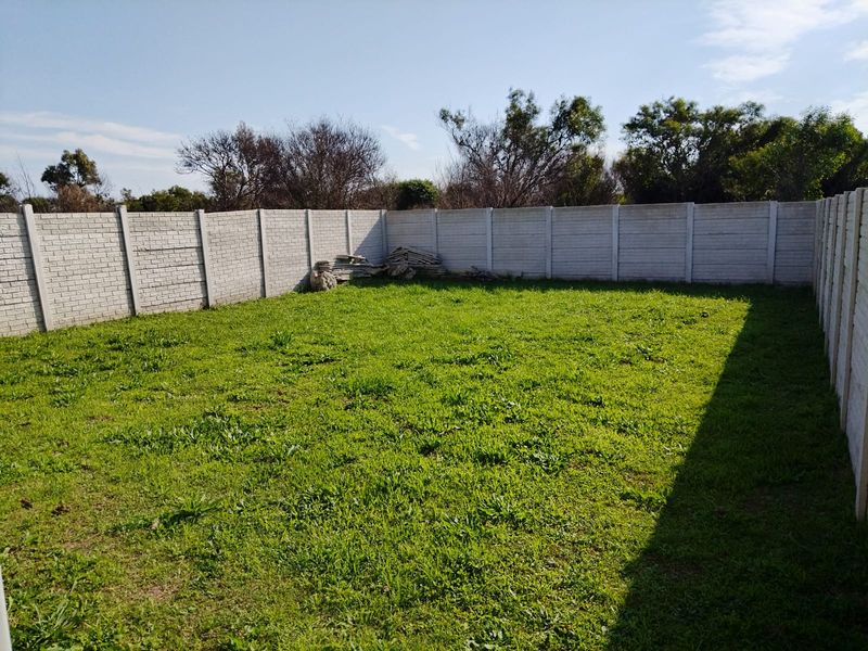 A spacious, enclosed backyard featuring a large lawn area surrounded by a precast concrete boundary wall.