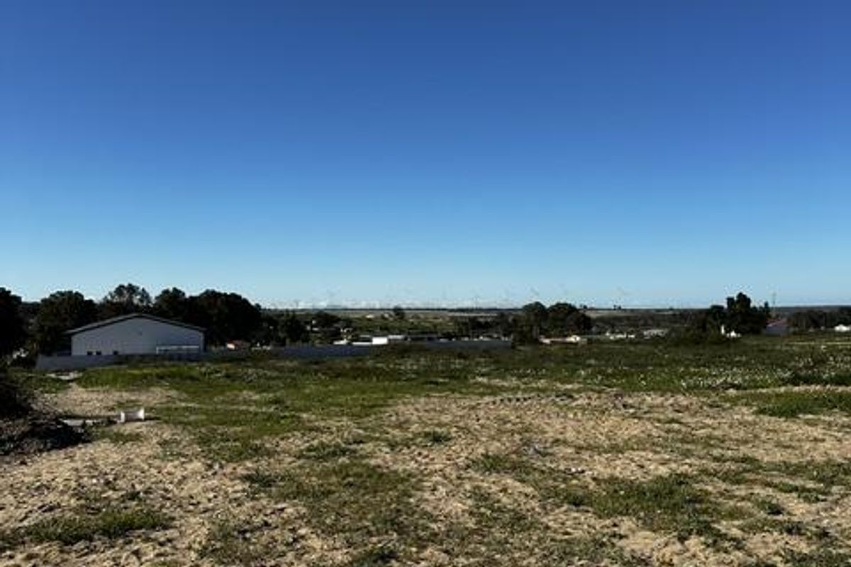 A wide-angle view of a vacant residential plot featuring natural ground cover and distant landscape views under a clear blue sky.