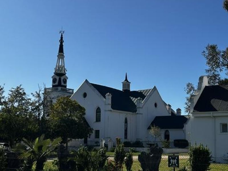 A view of a historic church building with a prominent spire and gabled roof, situated behind a landscaped verge.
