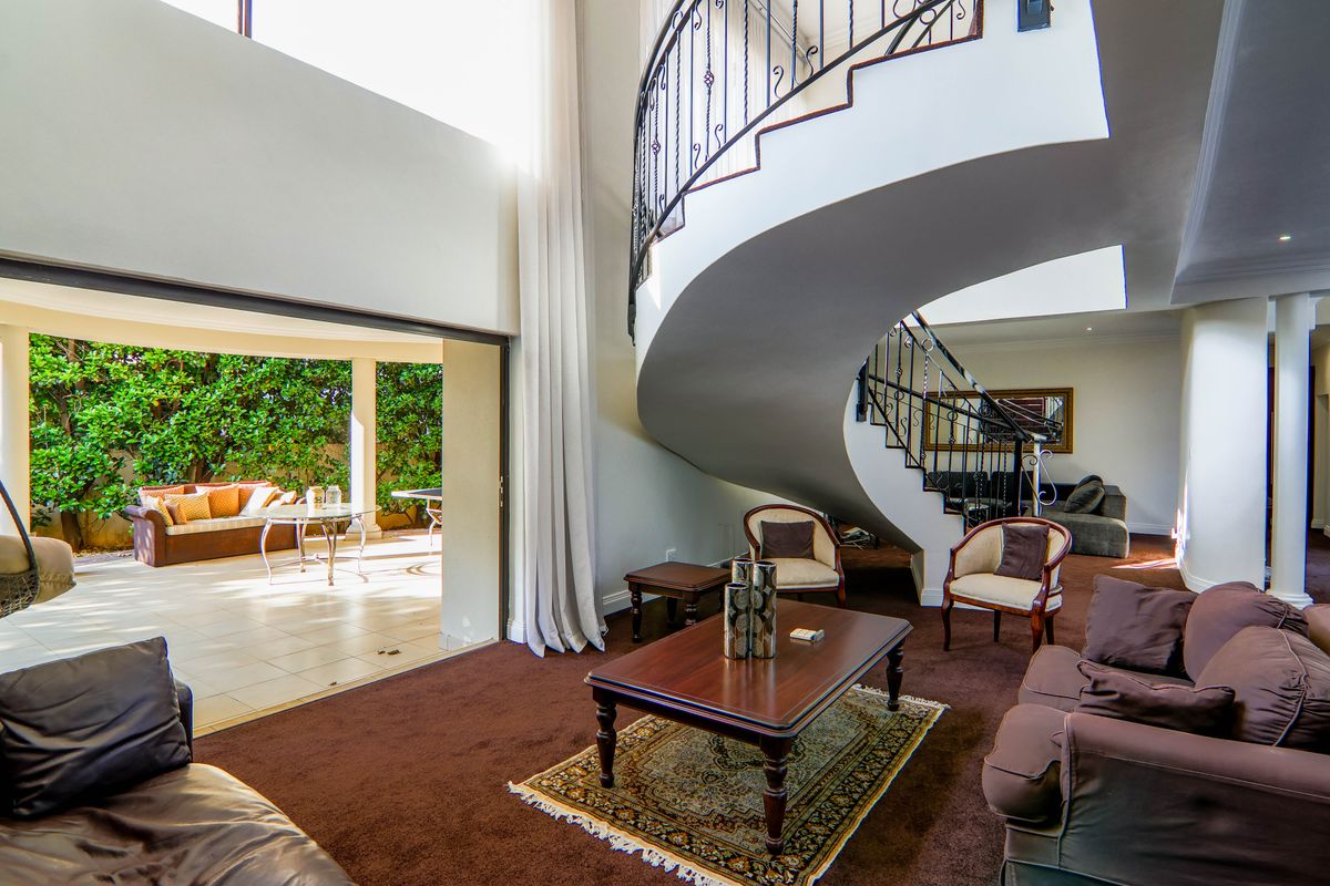 Spacious living area featuring a striking curved staircase with wrought iron balustrade and large sliding doors opening onto a covered patio.