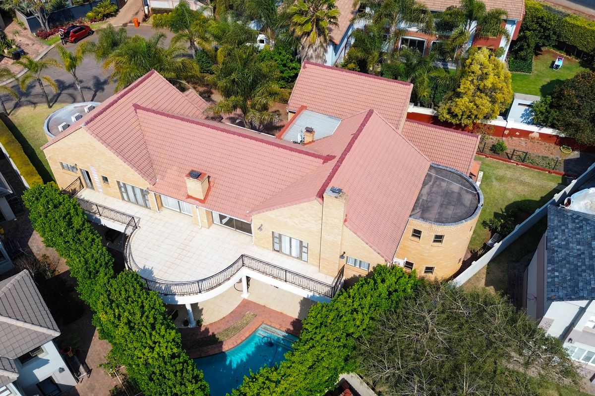 Aerial view of a large residential property featuring a tiled roof, a curved balcony, a swimming pool, and a paved patio area.