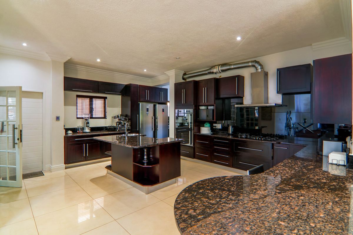 Spacious kitchen featuring dark wood cabinetry, granite countertops, a central island, and integrated appliances with modern recessed lighting and tiled flooring.