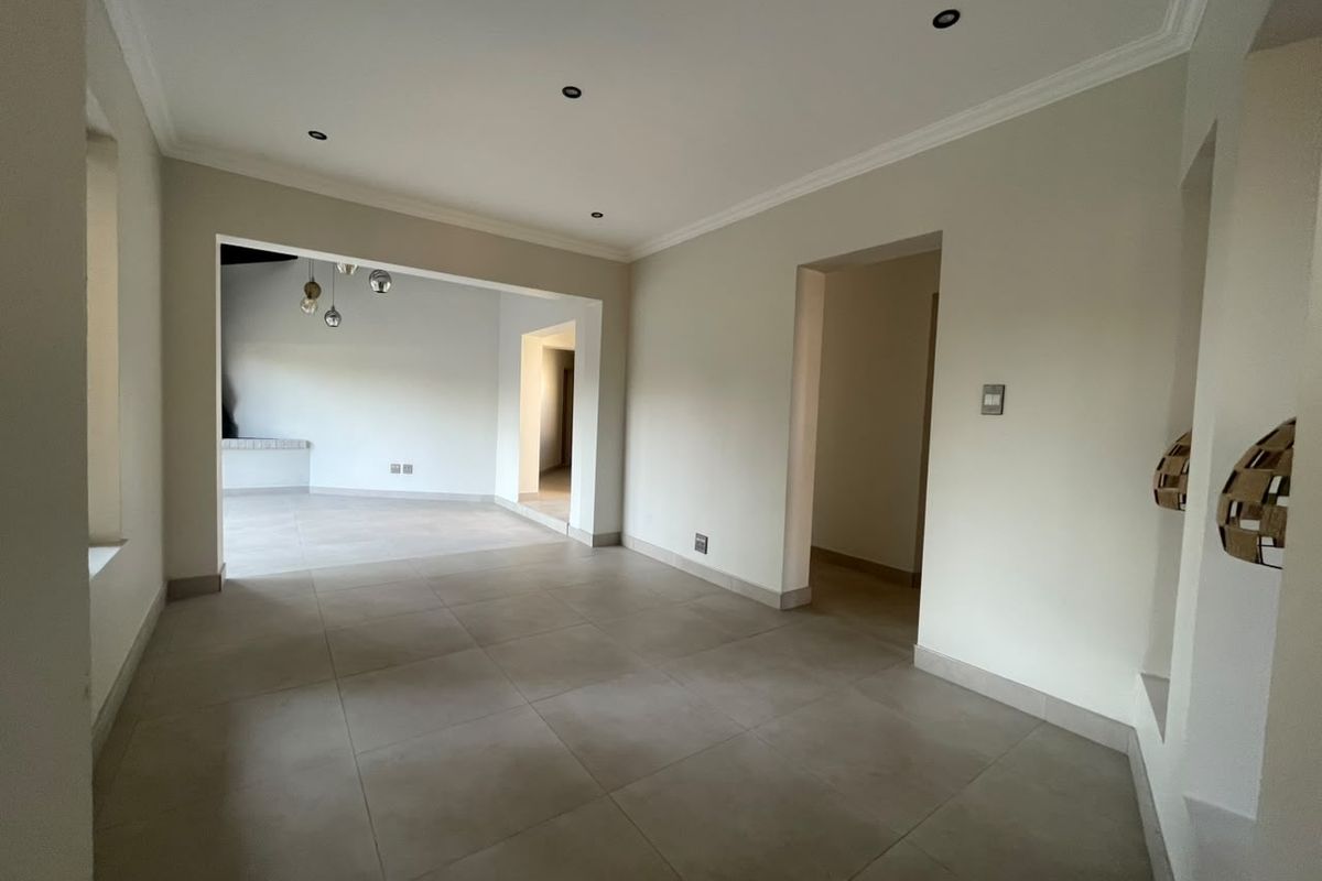 A spacious, empty living area featuring neutral tiled flooring, recessed downlighting, and coving, with an open-plan layout leading to adjacent rooms.