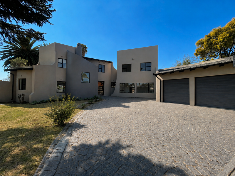 Front elevation of a modern house featuring a paved driveway, double garage, and distinctive architectural facade with clean lines.