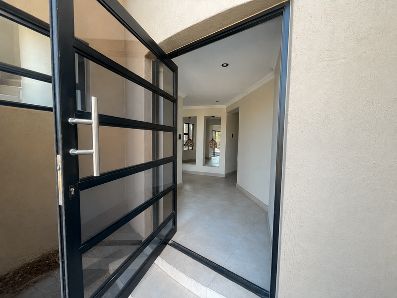 A bright and modern entrance hall featuring tiled flooring, recessed lighting, and a contemporary black-framed glass door.