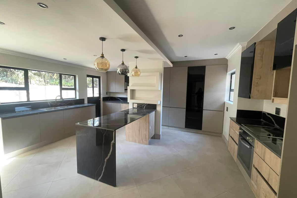 Modern, spacious kitchen featuring a large stone-topped island, sleek built-in cabinetry, integrated oven, and high-quality tiled flooring throughout.