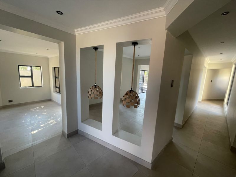 A bright, open-plan hallway featuring tiled flooring, decorative wall niches with pendant lighting, and neutral finishes throughout the interior space.