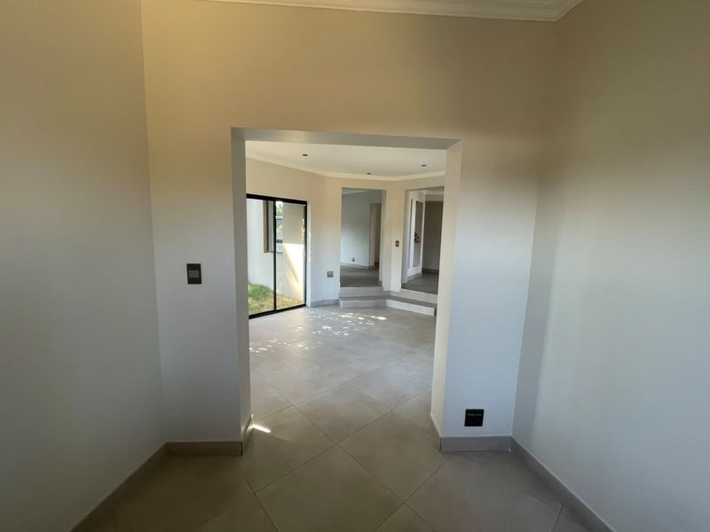 A bright, empty hallway featuring neutral tiled flooring and clean finishes, leading into an open-plan living area with natural light.